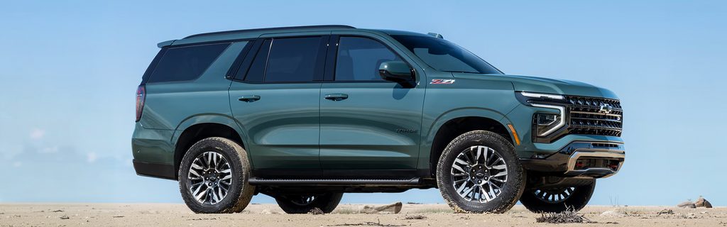 Dark green Chevrolet Tahoe parked on open sand.